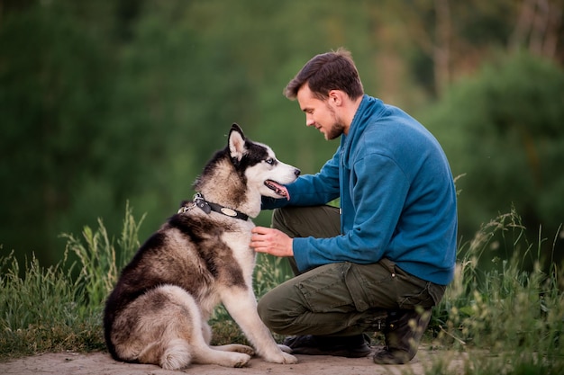 Portret van een knappe jonge man en zijn huisdier Siberische Husky hond in de natuur in de avond bij zonsondergang