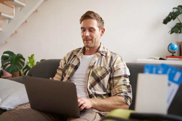 Portret van een knappe jonge man heeft twee kaartjes en paspoort gaat online op laptop hotel boeken en