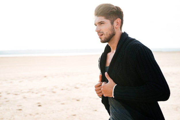 Portret van een knappe jonge man in vrijetijdskleding die op het strand loopt