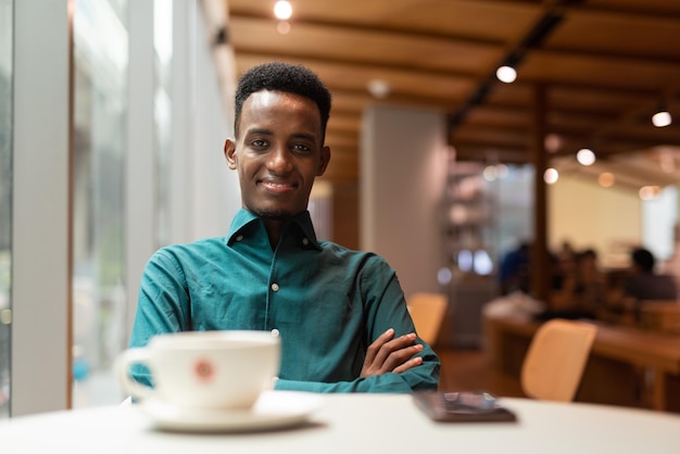 Portret van een knappe jonge zwarte man in een coffeeshop die naar de camera kijkt