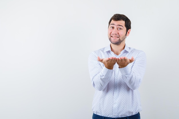 Portret van een knappe jongeman in een wit overhemd met patroon die wat service toont en er vrolijk uitziet, geïsoleerd op een witte achtergrond