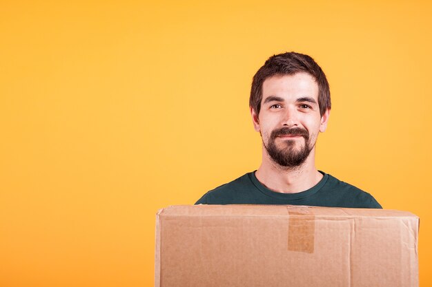 Portret van een knappe jongeman met een doos in zijn handen. Bezorger op gele achtergrond