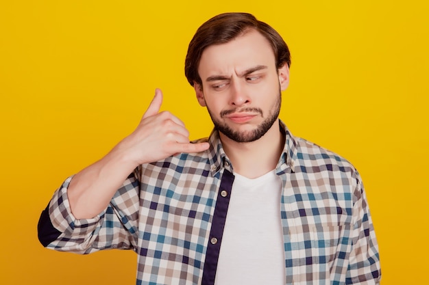 Portret van een knappe jongeman, ongelukkig, verdrietig, boos, negatief, toon vingeroproep, telefoonteken, geïsoleerd over gele kleurachtergrond