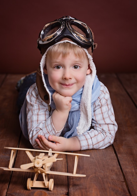 Foto portret van een knappe jongen in de helm van een piloot en blauwe sjaal met een houten vliegtuig