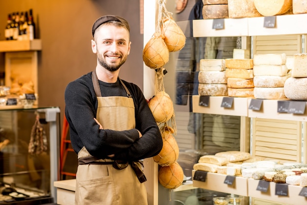 Portret van een knappe kaasverkoper in uniform bij de vitrine vol verschillende kazen in de winkel