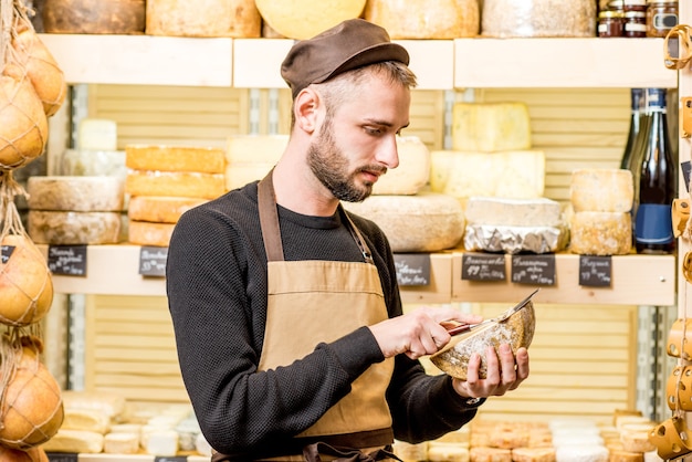 Portret van een knappe kaasverkoper in uniform die voor de winkelvitrine vol verschillende kazen staat