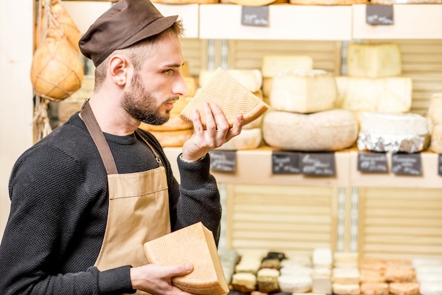 Portret van een knappe kaasverkoper in uniform ruikende gekruide kaas voor de winkelvitrine vol verschillende kazen