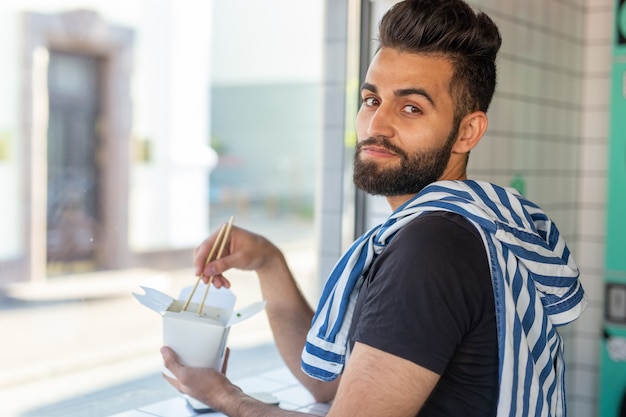 Portret van een knappe man chinese noedels eten in een café en kijkt uit het raam. het concept van een gezonde aziatische keuken.