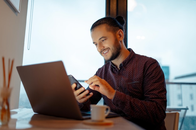 Foto portret van een knappe man die aan een laptop werkt op de achtergrond van een panoramisch raam