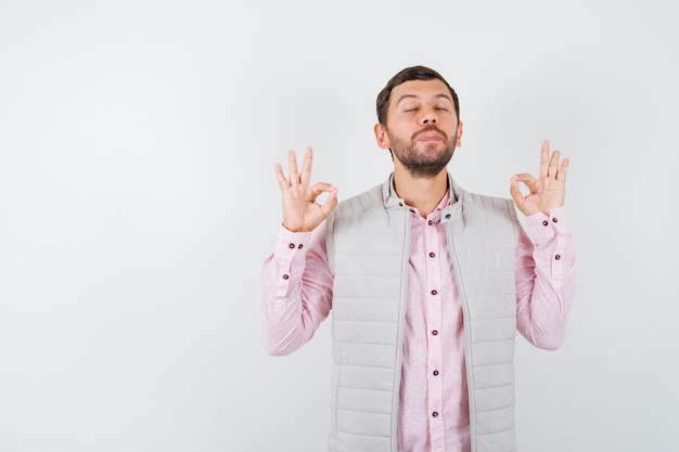 Portret van een knappe man die een meditatiegebaar in vest, shirt toont en er vredig uitziet