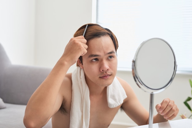 Portret van een knappe man die naar zichzelf in de spiegel kijkt en zijn haar borstelt.