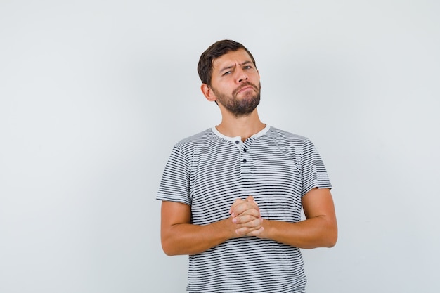 Foto portret van een knappe man die zijn vingers in een t-shirt geklemd houdt en er attent vooraanzicht uitziet
