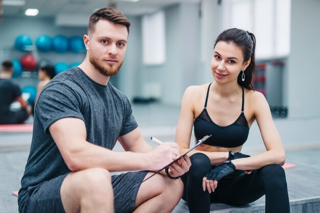 Portret van een knappe man en een aantrekkelijke vrouw die na training rusten en camera in sportengymnastiek onderzoeken.