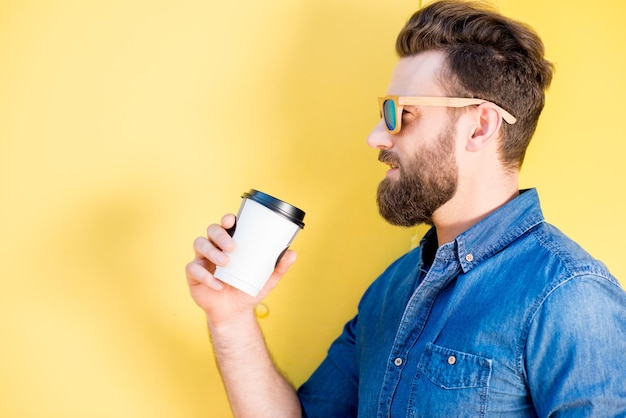 Portret van een knappe man in blauw t-shirt met koffie op de gele achtergrond