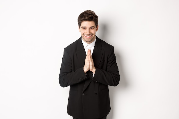 Portret van een knappe man in een zwart pak, dankbaar, bedankt en beleefd buigend, glimlachend als hand in hand, dankbaarheid uitdrukkend, staande op een witte achtergrond