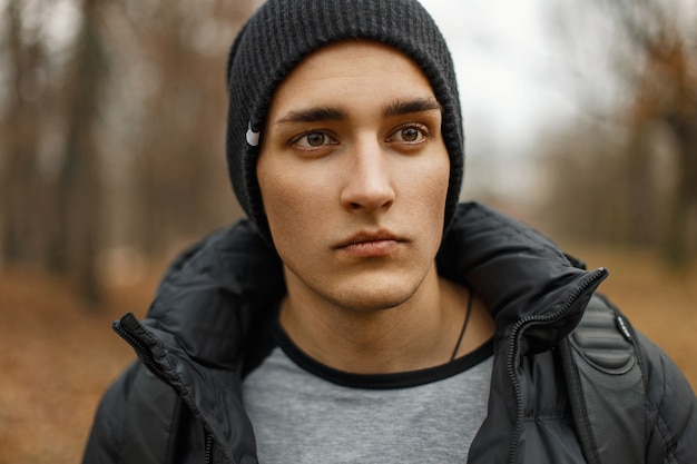 Portret van een knappe man in een zwarte gebreide muts en winterjas in het herfstpark