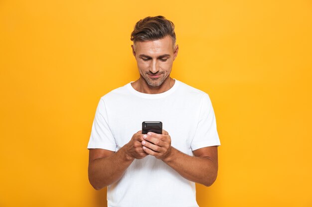 Portret van een knappe man poseren geïsoleerd op gele muur met behulp van mobiele telefoon.