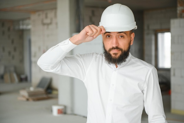 Portret van een knappe man uit het Midden-Oosten die een veiligheidshelm draagt en een bouwplan vasthoudt Werknemers en bedrijfsconcept