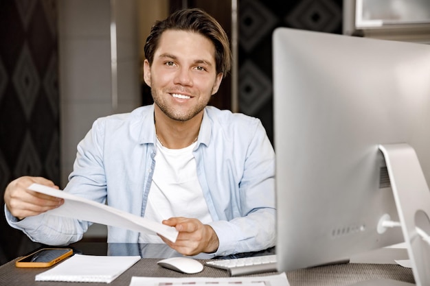 Portret van een knappe mannelijke freelancer zit aan het bureau en werkt in de verte in een thuiskantoor