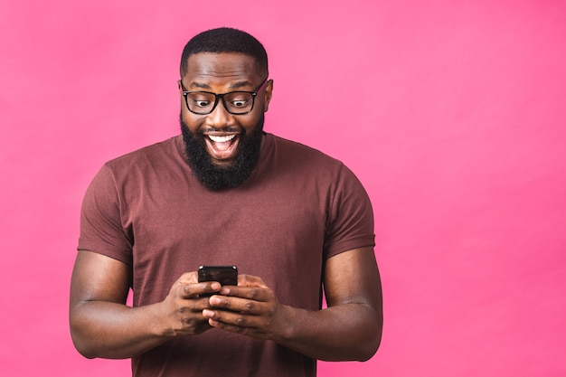 Portret van een knappe, opgewekte, vrolijke, heerlijke Afro-Amerikaanse zwarte man die casual berichten naar zijn geliefde verzendt en ontvangt, geïsoleerd over roze achtergrond. Telefoon gebruiken.