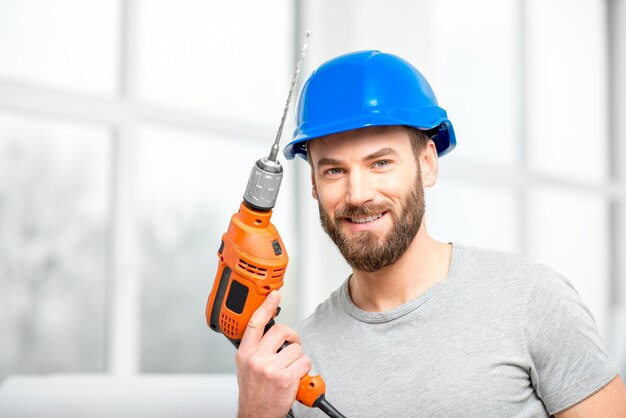 Portret van een knappe reparateur met boor en helm in het lichte interieur