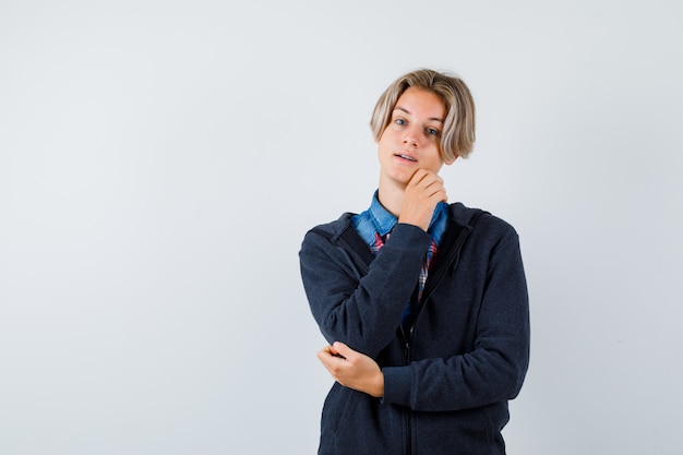 Portret van een knappe tienerjongen die zijn kin aanraakt in hemd, hoodie en er hoopvol vooraanzicht uitziet