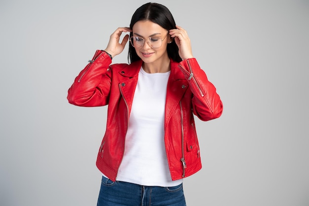 Portret van een knappe volwassen vrouw die haar donkerbruine haar corrigeert en neerkijkt voor de camera met een kalme uitdrukking gekleed in casual kleding geïsoleerd op een grijze studiomuur