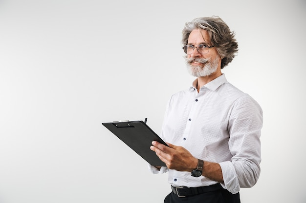 Portret van een knappe volwassen zakenman gekleed in formele kleding die geïsoleerd over een witte muur staat en aantekeningen maakt op notitieblok