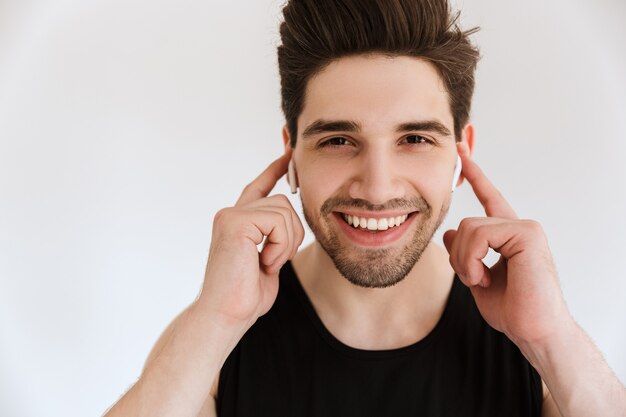 Portret van een knappe vrolijke lachende gelukkige jonge sportman geïsoleerd over witte muur luisteren muziek met oortelefoons.