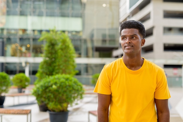 Portret van een knappe zwarte Afrikaanse man met een geel t-shirt buiten in de stad tijdens de zomer terwijl hij nadenkt