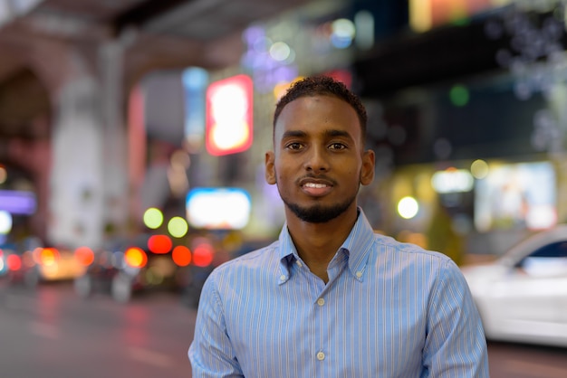 Portret van een knappe zwarte Afrikaanse zakenman buiten in de stad 's nachts glimlachend horizontaal schot?