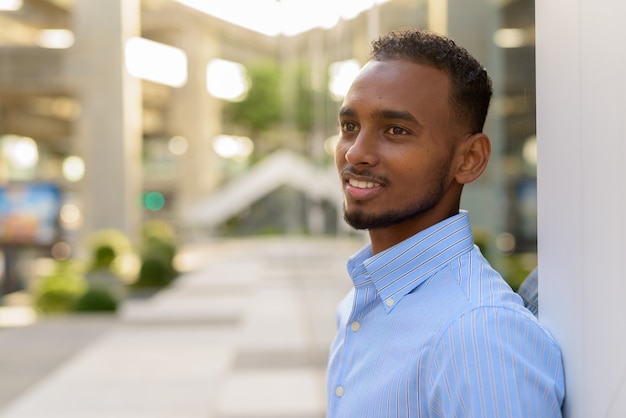 Portret van een knappe zwarte Afrikaanse zakenman buiten in de stad tijdens de zomer glimlachend en denkend