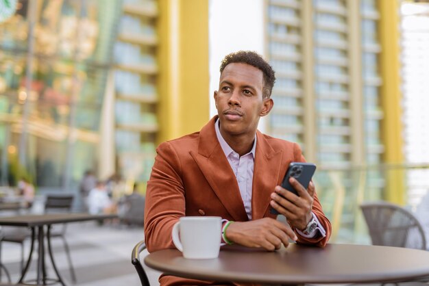 Portret van een knappe zwarte Afrikaanse zakenman die buiten in de coffeeshop zit met een mobiele telefoon