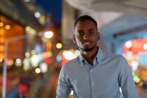 Portret van een knappe zwarte Afrikaanse zakenman die 's nachts buiten in de stad glimlacht en kijkt naar een horizontaal schot van de camera
