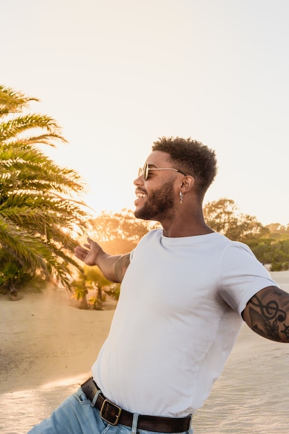 portret van een knappe zwarte Amerikaanse man die plezier heeft tijdens zonsondergang op het strand met palmen palm