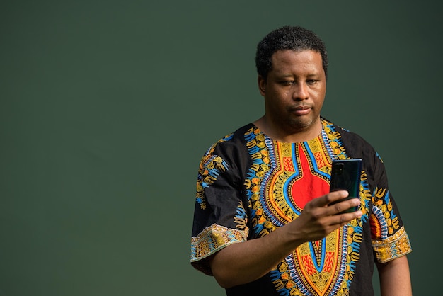 Foto portret van een knappe zwarte man die traditionele kleding draagt en een mobiele telefoon gebruikt