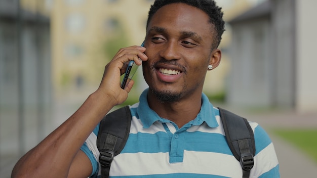 Portret van een knappe zwarte man met een telefoongesprek in de buitenlucht glimlachende Afro-Amerikaanse man die smartphone gebruikt