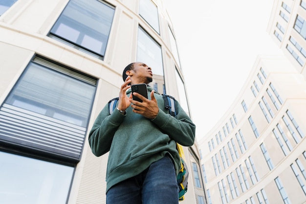 Portret van een koerier met een gele rugzak met een smartphone op de achtergrond van een modern glazen gebouw