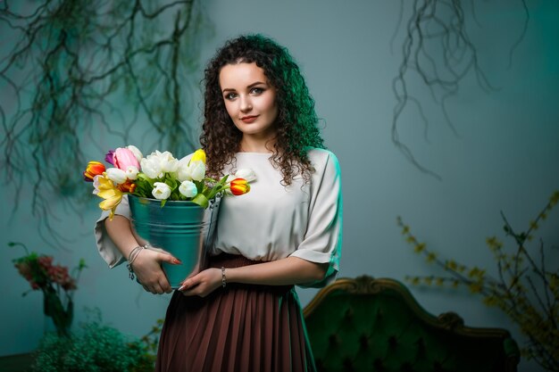 Portret van een krullend meisje met een emmer tulpen. Verse bloemen voor mooie foto's. Delicate foto's met bloemen in de studio