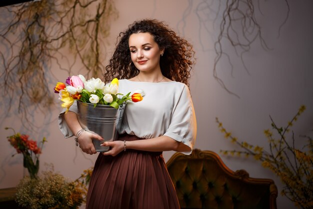 Portret van een krullend meisje met een emmer tulpen. Verse bloemen voor mooie foto's. Delicate foto's met bloemen in de studio