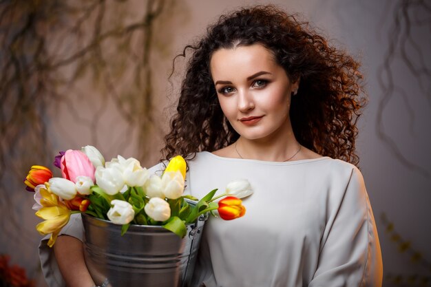 Portret van een krullend meisje met een emmer tulpen. Verse bloemen voor mooie foto's. Delicate foto's met bloemen in de studio