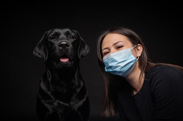 Portret van een Labrador Retriever-hond met een beschermend medisch masker met een vrouwelijke eigenaar