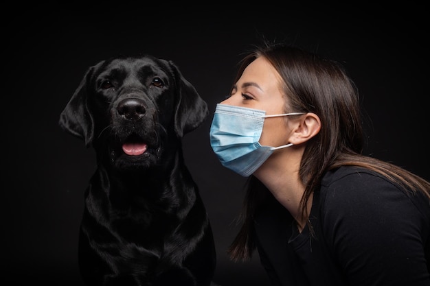 Portret van een Labrador Retriever-hond met een beschermend medisch masker met een vrouwelijke eigenaar