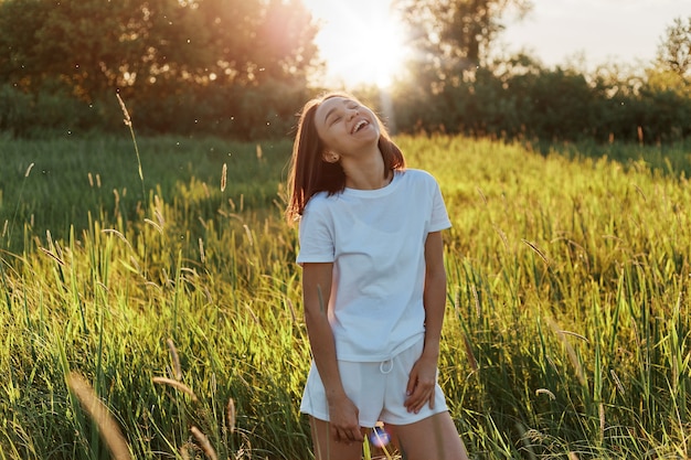 Portret van een lachend donkerharig meisje dat een casual stijl draagt, een vrouw met een brede glimlach die geniet van de zomer, tijd doorbrengt in een groen veld, frisse lucht inademt.