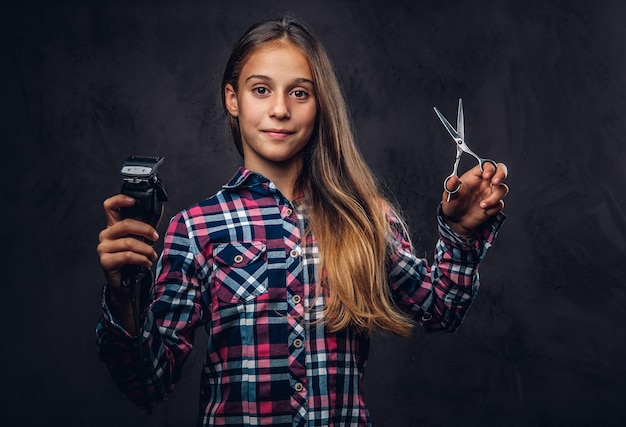 Portret van een lachend jong meisje gekleed in shirt houdt trimmer en schaar. Geïsoleerd op een donkere gestructureerde achtergrond.