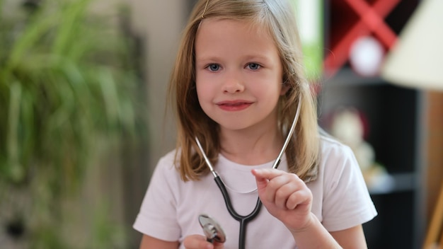 Portret van een lachend meisje dat een medische stethoscoop gebruikt en met de vinger naar iemand wijst