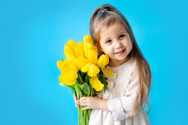 Portret van een lachend meisje een kind met een boeket gele tulpen op een blauwe geïsoleerde achtergrond Lifestyle International Women's of Mother's Day Ruimte voor tekst Hoogwaardige fotografie