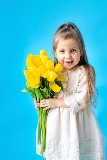 Portret van een lachend meisje een kind met een boeket gele tulpen op een blauwe geïsoleerde achtergrond lifestyle international women's of mother's day ruimte voor tekst hoogwaardige fotografie