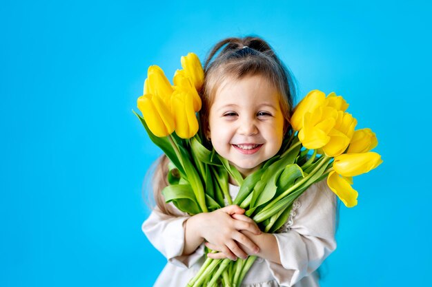 Portret van een lachend meisje een kind met een boeket gele tulpen op een blauwe geïsoleerde achtergrond Lifestyle International Women's of Mother's Day Ruimte voor tekst Hoogwaardige fotografie