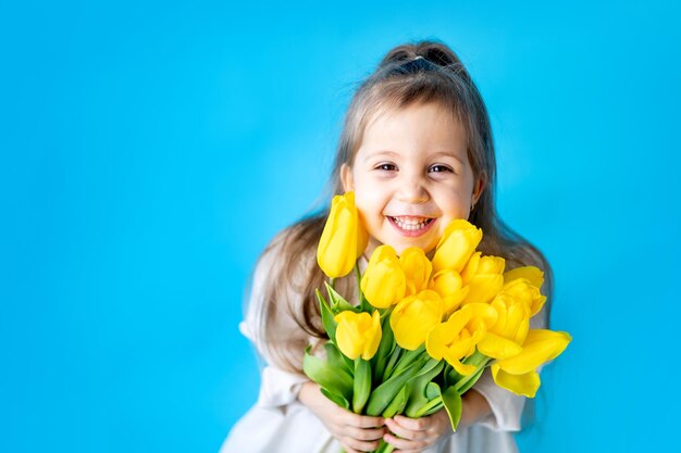 Portret van een lachend meisje een kind met een boeket gele tulpen op een blauwe geïsoleerde achtergrond Lifestyle International Women's of Mother's Day Ruimte voor tekst Hoogwaardige fotografie